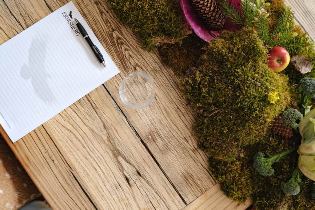 Noted on paper with pen, plant arrangement and glass on wooden table.