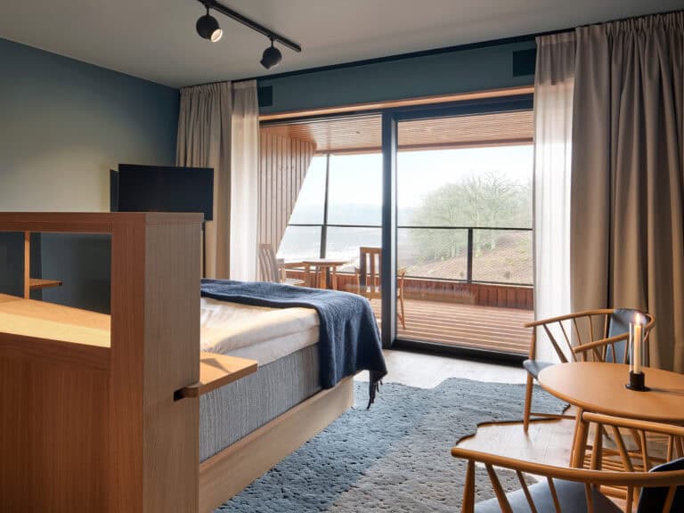 Modern hotel room with balcony, large window, and wooden furniture at Eriksberg.